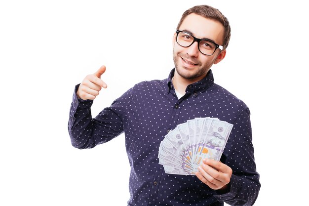 Retrato de un hombre confiado serio sosteniendo un montón de billetes de banco y señalando con el dedo al frente aislado sobre la pared blanca