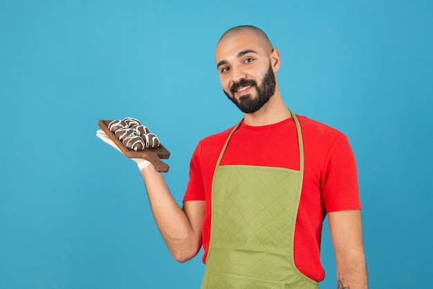 Retrato de un hombre en delantal sosteniendo una tabla de madera con galletas recubiertas de chocolate.