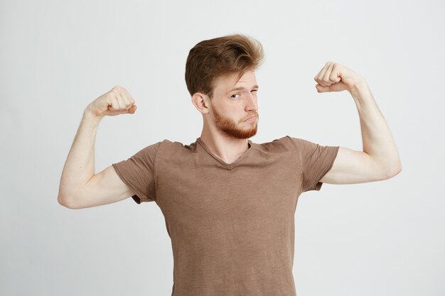 Retrato del hombre deportivo sano joven que muestra los músculos del bíceps que se jactan mirando la cámara.