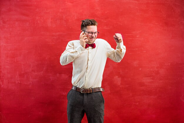 Retrato de hombre desconcertado con gafas hablando por teléfono en un estudio rojo