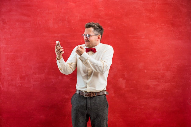 Retrato de hombre desconcertado con gafas hablando por teléfono sobre un fondo rojo de estudio