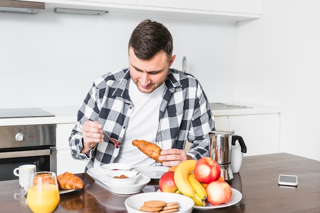 Foto gratuita retrato de un hombre disfrutando del croissant en la cocina.