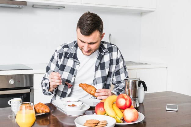 Retrato de un hombre disfrutando del croissant en la cocina.