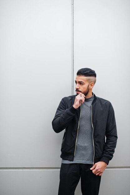 Retrato de un hombre elegante con barba árabe que usa un cuello alto gris y un modelo árabe jaket negro contra una pared de acero