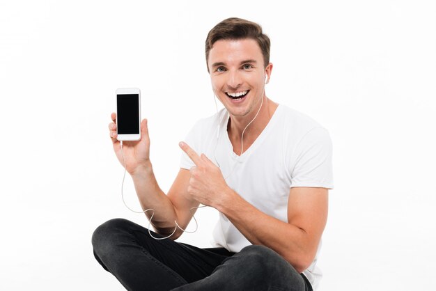 Retrato de un hombre emocionado feliz en auriculares apuntando con el dedo