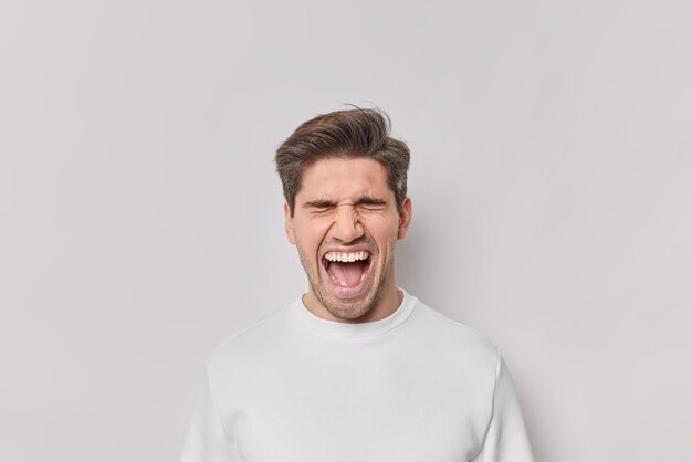 El retrato de un hombre emotivo grita de asombro mantiene la boca abierta grita en voz alta usa un puente casual aislado sobre fondo blanco. Modelo masculino emocionado reacciona ante noticias increíbles o sorpresa