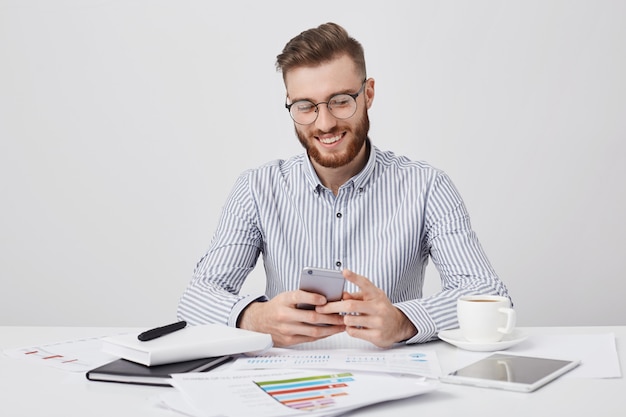 Retrato de hombre encantador con barba incipiente y peinado de moda, charla con su novia a través de las redes sociales tiene aspecto feliz,