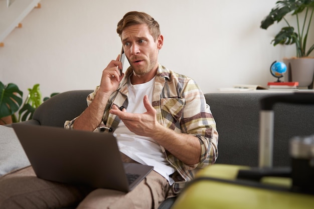 Foto gratuita retrato de un hombre enojado que parece frustrado hablando por teléfono móvil sentado con una computadora portátil y una maleta