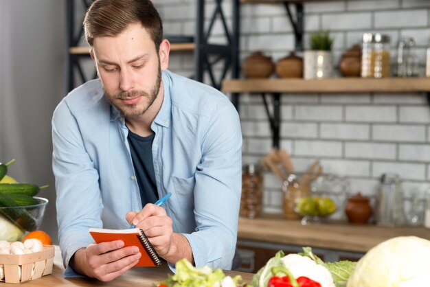 Retrato de un hombre escribiendo una receta en su diario en la cocina.