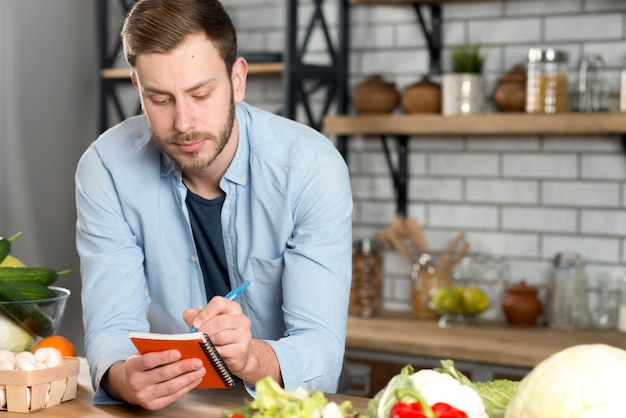 Retrato de un hombre escribiendo una receta en su diario en la cocina.