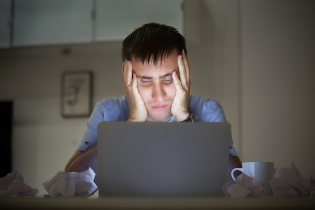 Retrato de un hombre en el escritorio cerca de portátil, por la noche