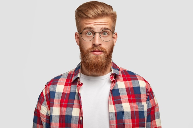 Retrato de hombre con estilo pelirrojo aturdido en gafas y camisa a cuadros, se ve sorprendentemente