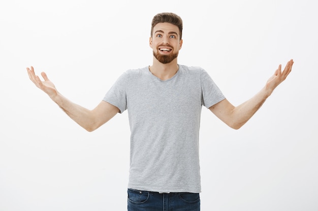 Retrato de hombre europeo sorprendido y emocionado sorprendido con barba y levantando las manos al aire con aspecto alegre y agradecido dando gracias a Dios por ayudarlo a cumplir sus deseos y sueños sobre la pared gris