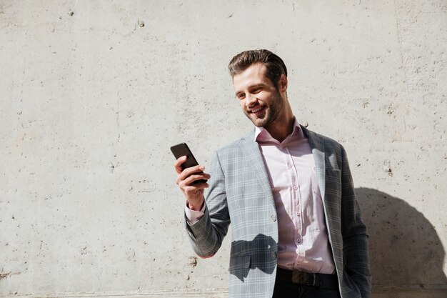 Retrato de un hombre feliz en chaqueta con teléfono móvil