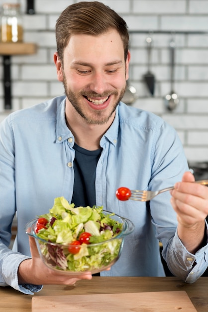 Foto gratuita retrato de un hombre feliz comiendo ensalada fresca saludable en el tazón de fuente