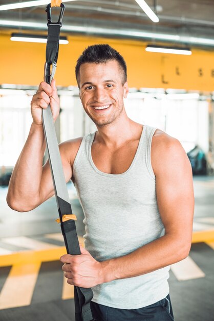 Retrato de un hombre feliz con correa de fitness en gimnasio