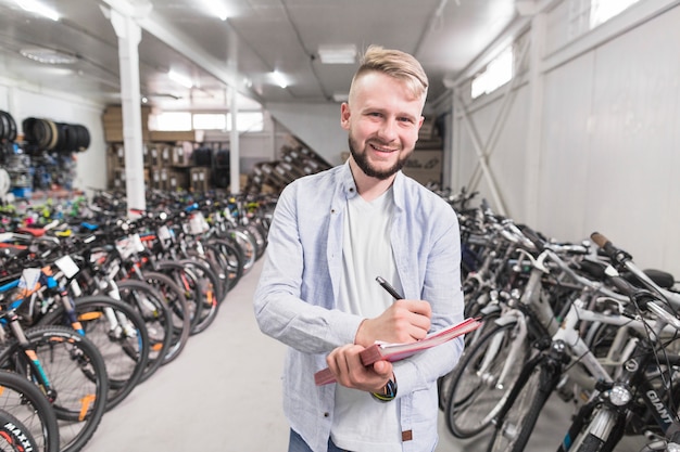 Retrato de un hombre feliz escribiendo en el documento en la tienda de bicicletas