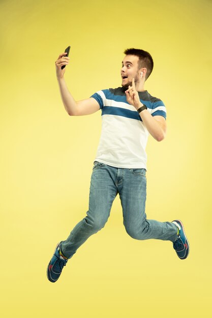 Retrato de hombre feliz saltando con gadgets en pared amarilla