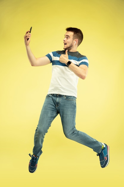 Retrato de hombre feliz saltando con gadgets en pared amarilla