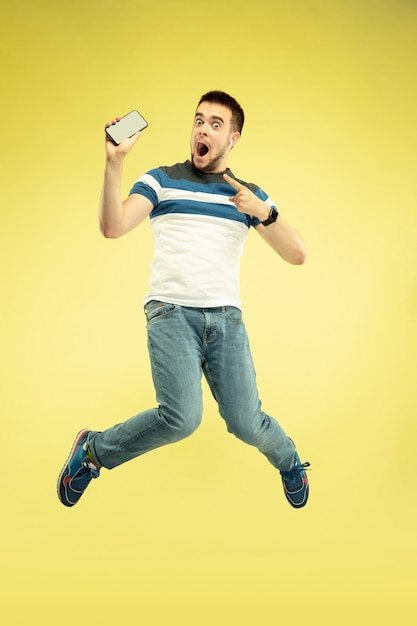 Retrato de hombre feliz saltando con gadgets en pared amarilla