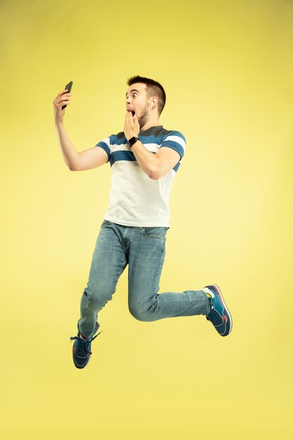 Retrato de hombre feliz saltando con gadgets en pared amarilla