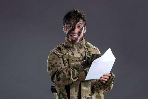 Retrato de hombre feliz soldado en camuflaje leyendo carta en pared oscura