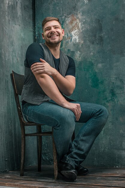 Retrato de hombre feliz sonriente sentado en la silla de madera en estudio gris