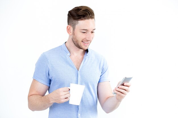 Retrato del hombre feliz con la taza usando el smartphone