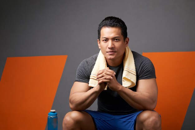 Retrato de hombre en forma con los dedos entrelazados sentados en el sofá del gimnasio después del entrenamiento