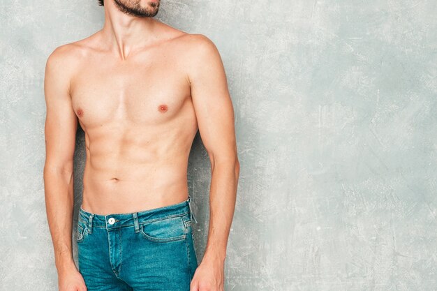 Retrato de hombre fuerte guapo deportivo. Modelo de fitness atlético saludable posando junto a la pared gris en jeans.