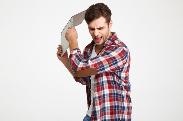 Retrato de un hombre furioso enojado lanzando su computadora portátil