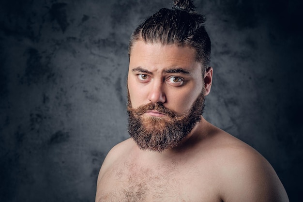 Retrato de un hombre gordo y barbudo sin camisa sobre fondo gris.