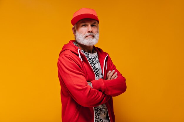 Retrato de hombre de gorra roja y sudadera con capucha en pared naranja