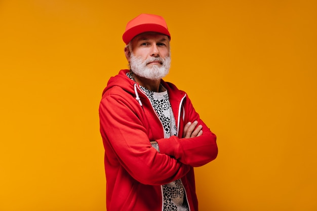 Retrato de hombre de gorra roja y sudadera con capucha en pared naranja