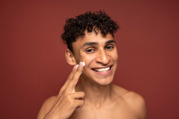 Foto gratuita retrato de un hombre guapo aplicando crema hidratante en su rostro y sonriendo