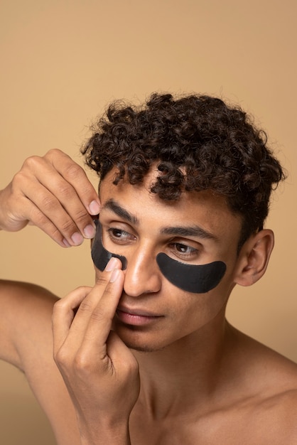 Retrato de un hombre guapo aplicando parches de carbón debajo de los ojos