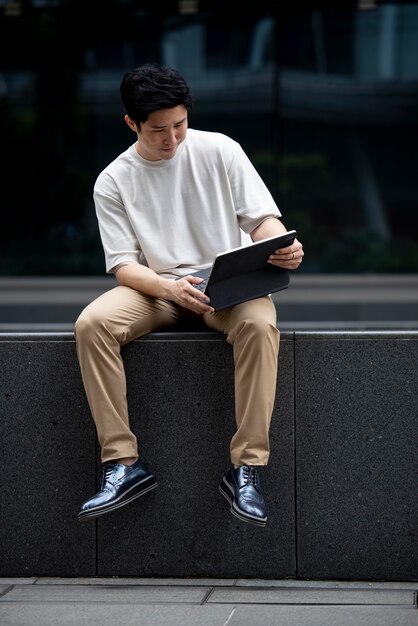 Retrato de hombre guapo asiático usando laptop al aire libre en la ciudad