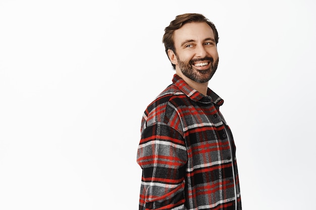 Retrato de un hombre guapo con barba de 35 años mirando hacia atrás en el espacio vacío promocional sonriendo y riendo de pie sobre fondo blanco