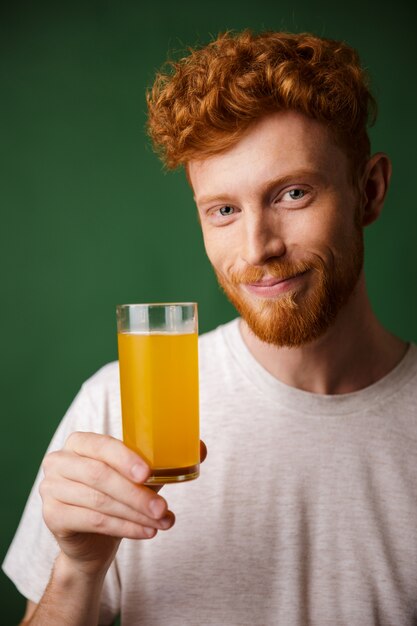 Retrato de hombre guapo con barba sonriente sosteniendo un vaso de jugo de naranja