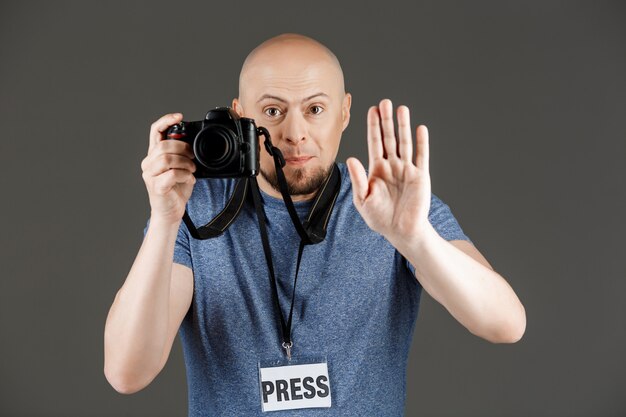 Retrato de hombre guapo en camisa gris con cámaras fotográficas y placa de prensa tomando fotos sobre la pared oscura