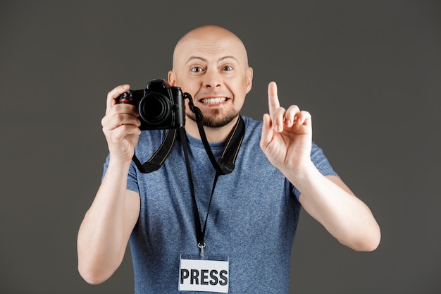 Retrato de hombre guapo en camisa gris con cámaras fotográficas y placa de prensa tomando fotos sobre la pared oscura