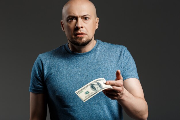 Retrato de hombre guapo en camisa gris con dinero sobre la pared oscura