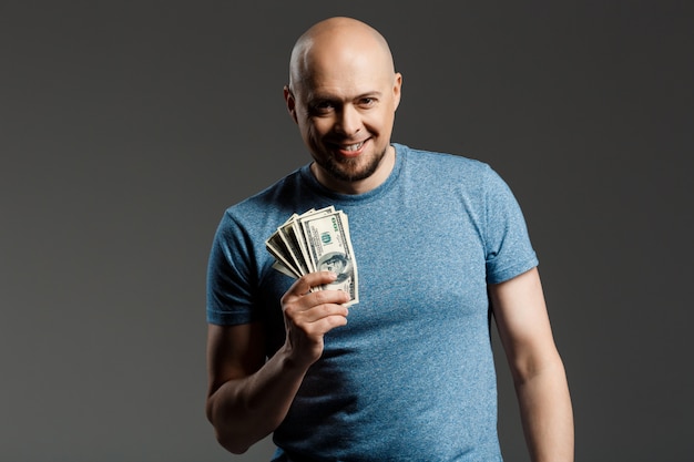 Retrato de hombre guapo en camisa gris con dinero sobre la pared oscura