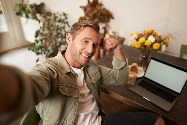 Foto gratuita retrato de un hombre guapo y confiado tomando una selfie flexionando los bíceps para mostrar sus músculos