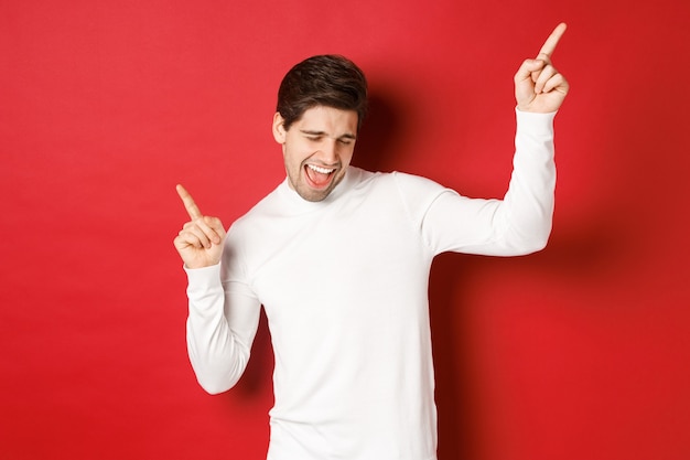 Retrato de hombre guapo disfrutando de fiesta de año nuevo bailando y divirtiéndose señalando con el dedo de pie ...