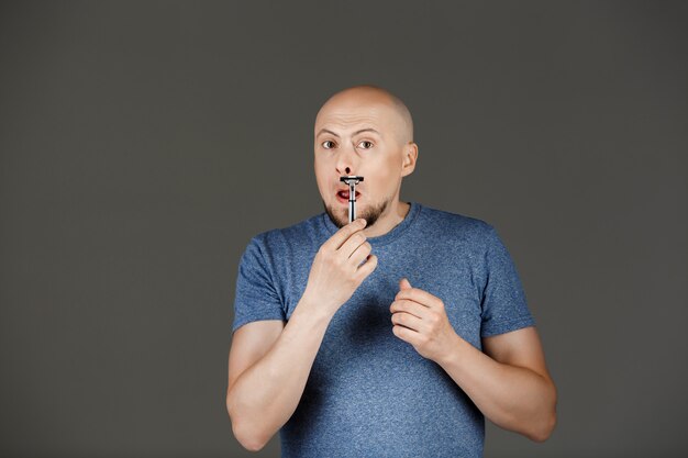 Retrato de hombre guapo divertido en camisa gris afeitado sobre pared oscura