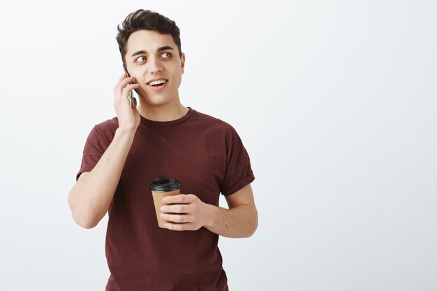 Retrato de hombre guapo intrigado en camiseta roja hablando por teléfono
