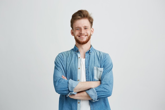 Retrato de hombre guapo joven en camisa de jean sonriendo con los brazos cruzados.