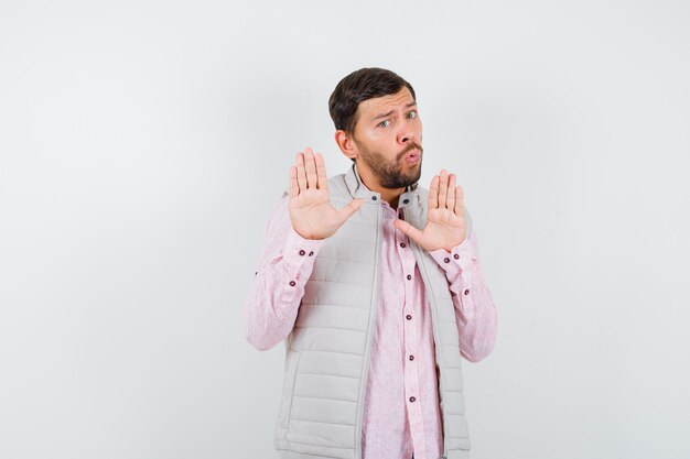 Retrato de hombre guapo mostrando palmas en gesto de rendición en chaleco, camisa y mirando aterrorizado