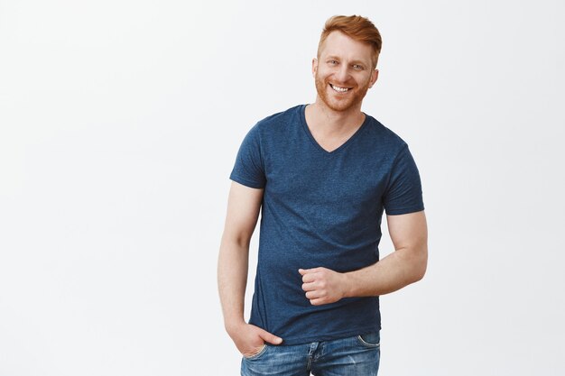 Retrato de hombre guapo pelirrojo masculino en camiseta azul, gesticulando y sonriendo ampliamente